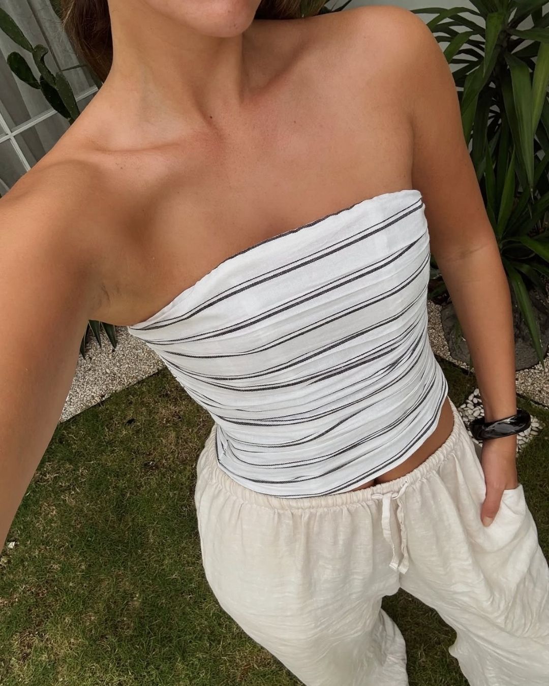 Person wearing a strapless white top with black stripes and white pants outdoors.
